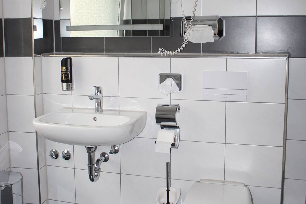 Un bagno con un lavandino bianco, uno specchio, un water e un asciugacapelli a parete.