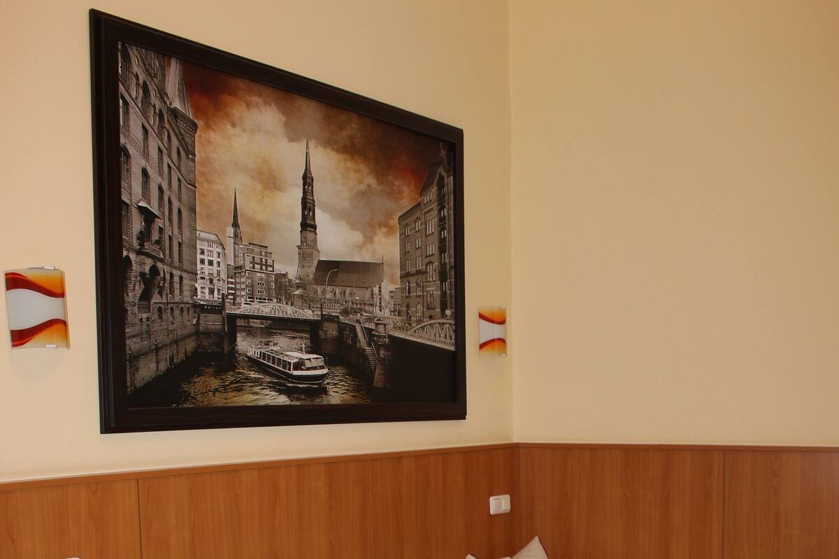 Camera d'albergo con tre letti, una testiera in legno e un grande quadro raffigurante un panorama cittadino.