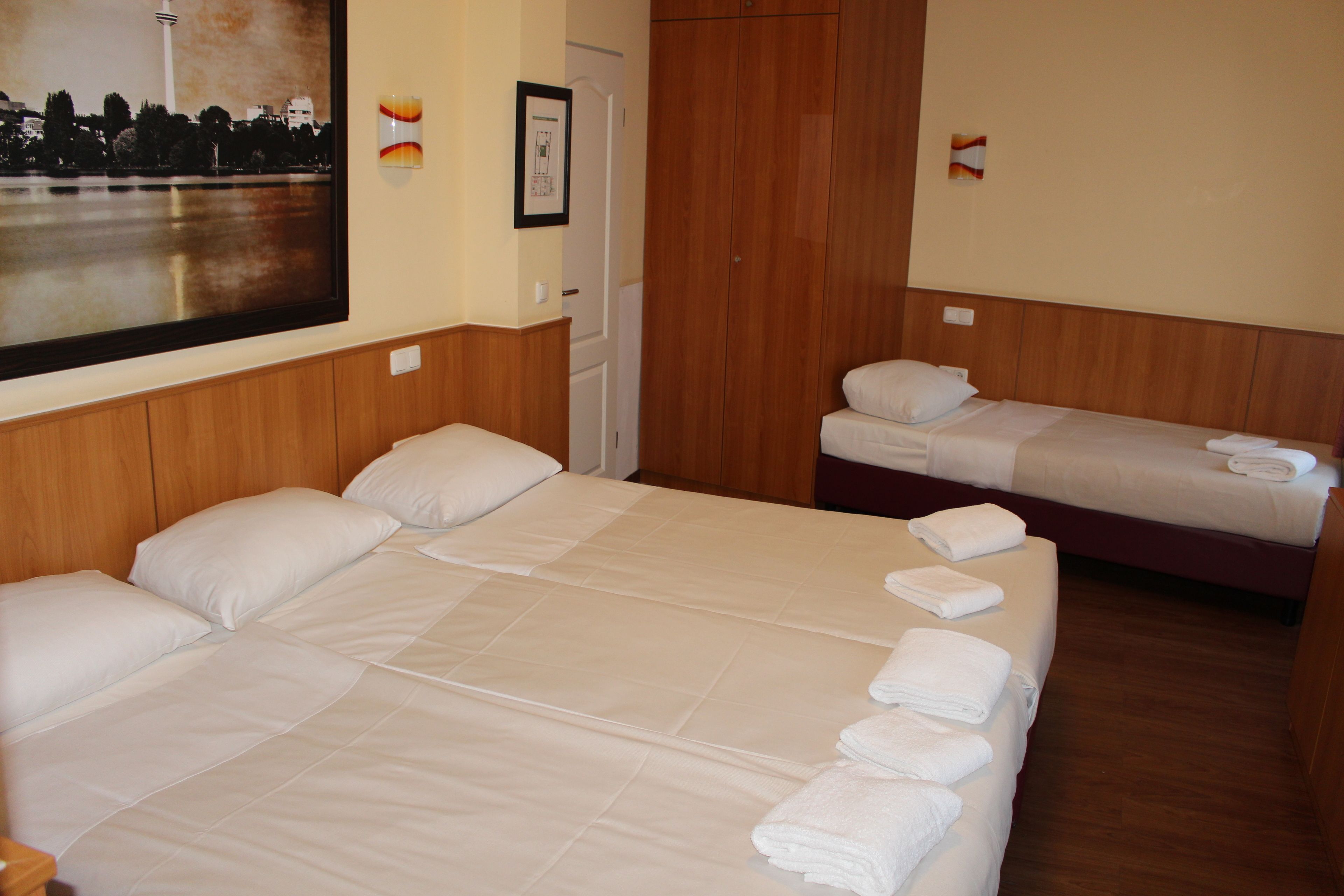 A hotel room with a large bed, a smaller bed, and a wooden wardrobe.