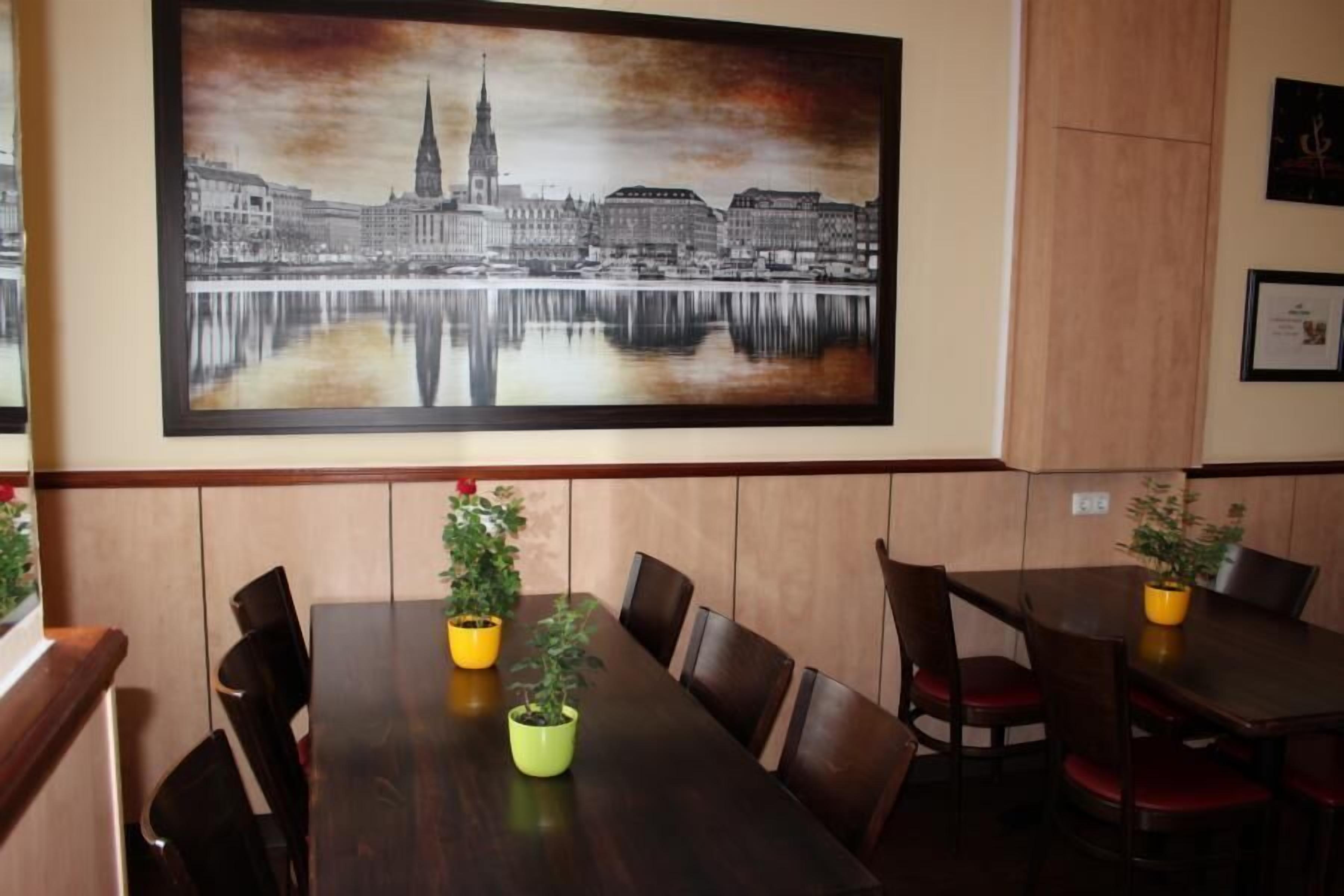 Un espace repas agrémenté d’un grand tableau représentant un paysage urbain au mur, de tables et de chaises en bois.