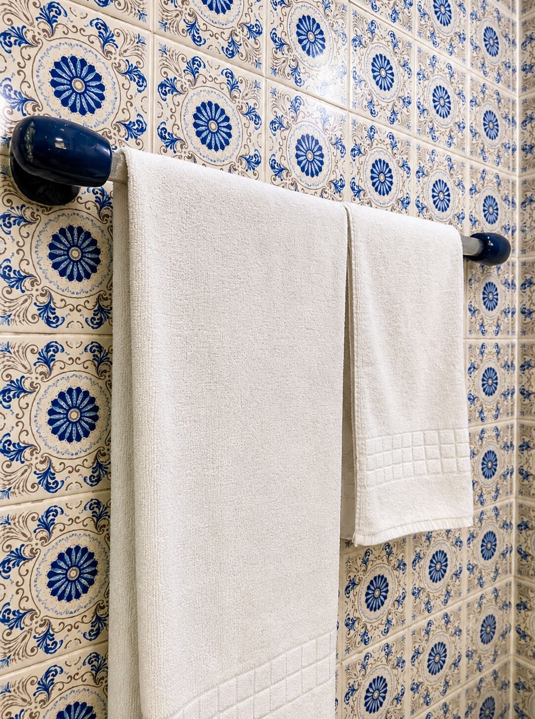 A bathroom with patterned tiles and two towels hanging on a rack.