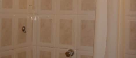 A shower with a white curtain, tiled walls, and a handheld showerhead.