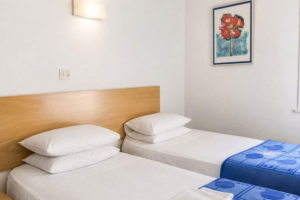 A hotel room with two beds, a nightstand, a wall-mounted light, and a framed artwork.