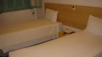 Quarto com duas camas de solteiro, cada uma com cabeceira de madeira e roupa de cama branca.