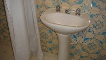 Un baño con un lavamanos blanco, azulejos con diseño azul y beige, y una cortina de ducha blanca.