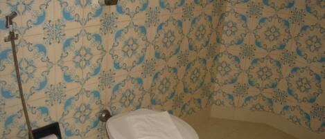 Un baño con inodoro, ducha y dispensador de toallas en la pared.