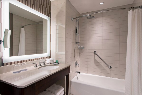 A modern bathroom with a large mirror, two sinks, a shower with a grab bar, and a bathtub. - The Westin Wilmington (Wilmington)