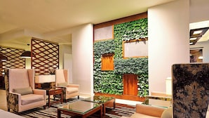 A modern lobby with a sectional sofa, a glass coffee table, and a decorative wall with greenery and geometric patterns.