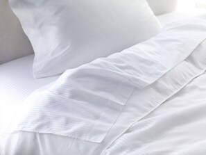 Primer plano de ropa de cama blanca con textura suave y un sutil patrón de sija.