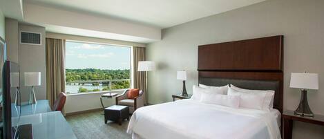 Habitación de hotel con una cama grande, un escritorio, una silla y vistas a un puente y zonas verdes.