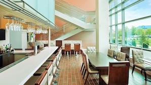 A modern restaurant with a bar area, seating with high backs, and large windows offering a view of the outdoors.