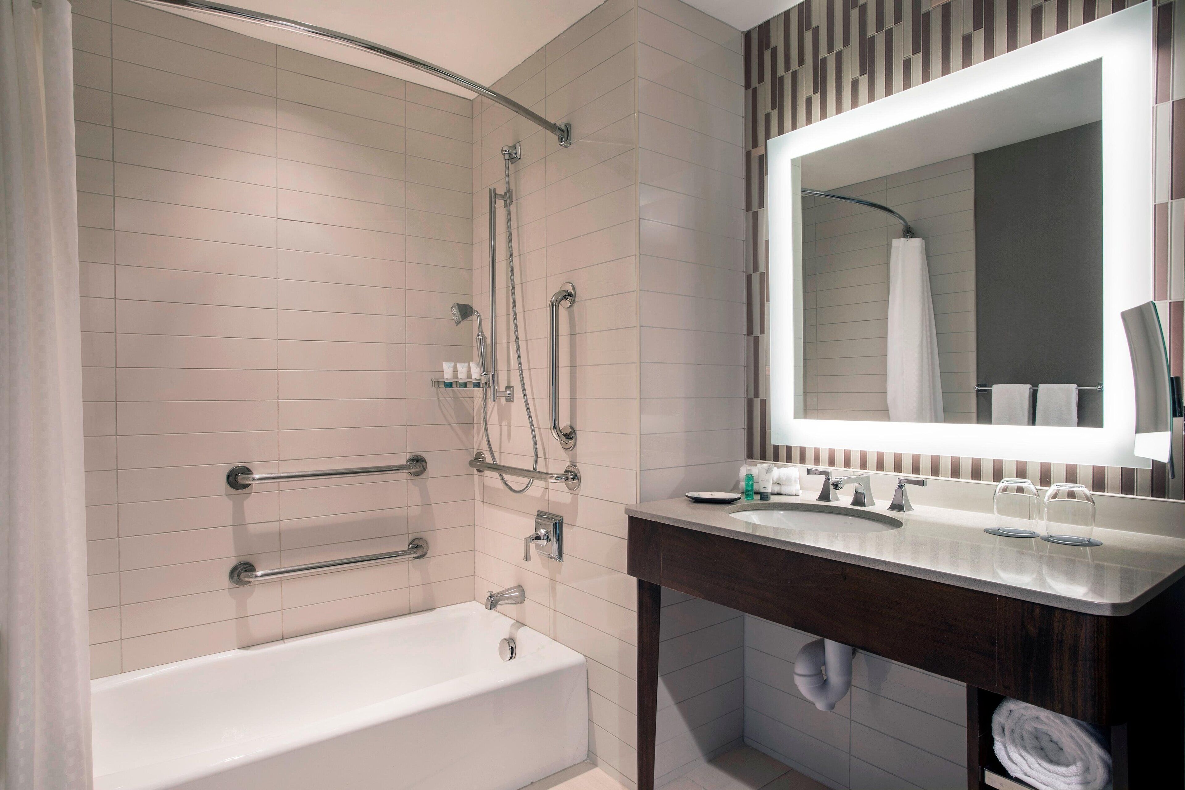 Un baño moderno con bañera, ducha con barras de apoyo, tocador con espejo y toallero.