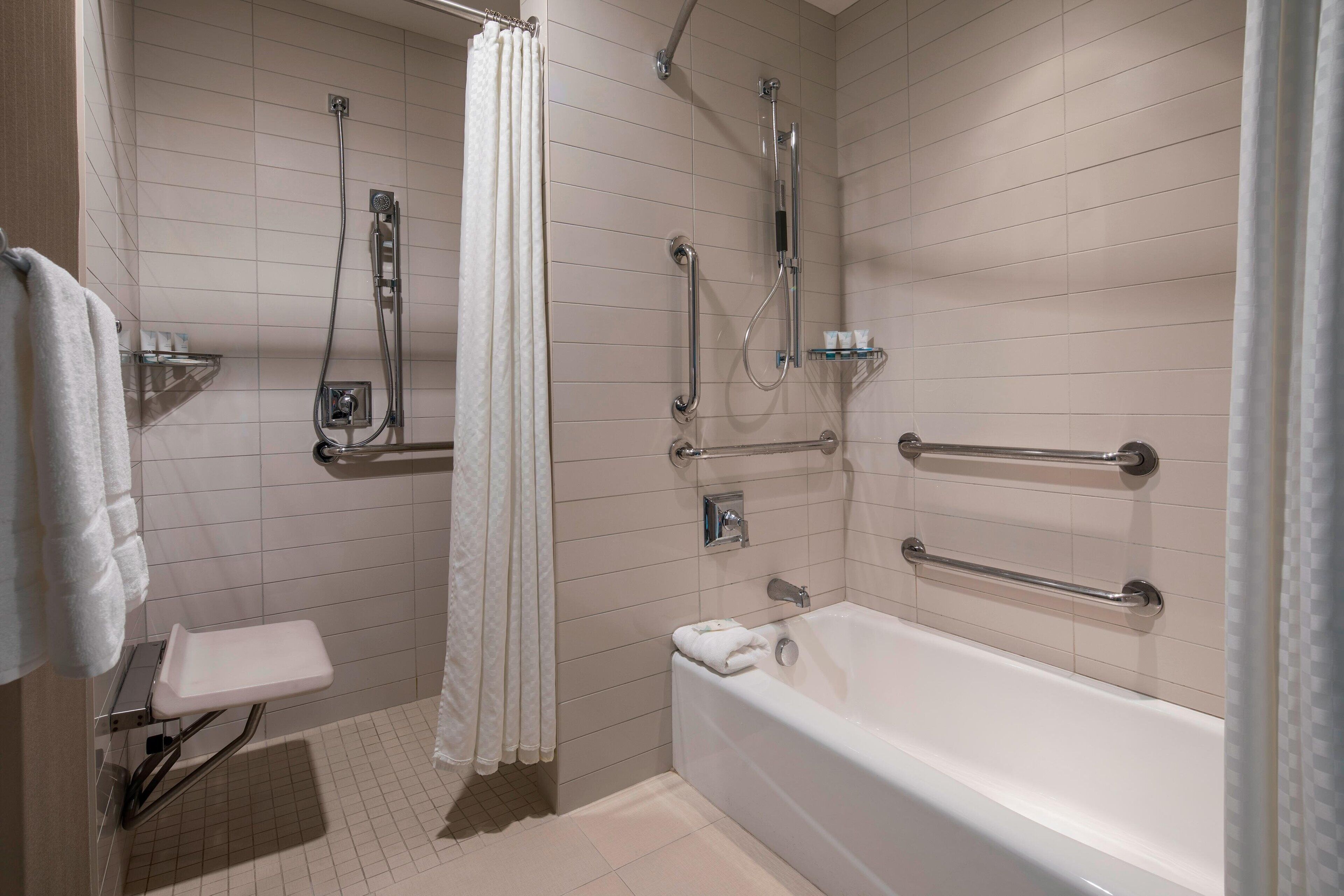 Een moderne badkamer met een inloopdouche, greepstangen, een badkuip en een toilet met een veiligheidsgreep.