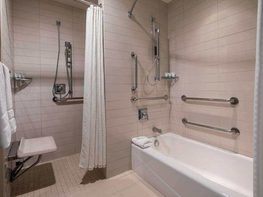 Een moderne badkamer met een inloopdouche, greepstangen, een badkuip en een toilet met een veiligheidsgreep.