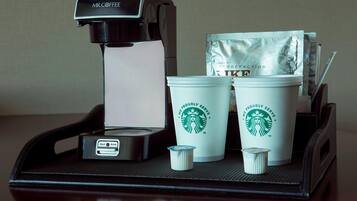Una cafetera, dos tazas de Starbucks y un paquete de cápsulas de café sobre una bandeja.