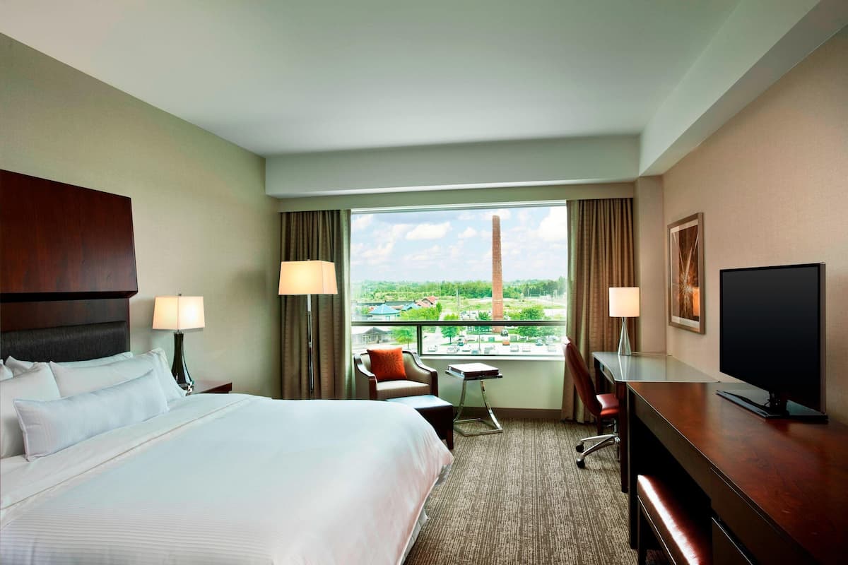 Una habitación de hotel con una cama grande, dos sillas, un escritorio con televisor y una ventana con vista a la ciudad.