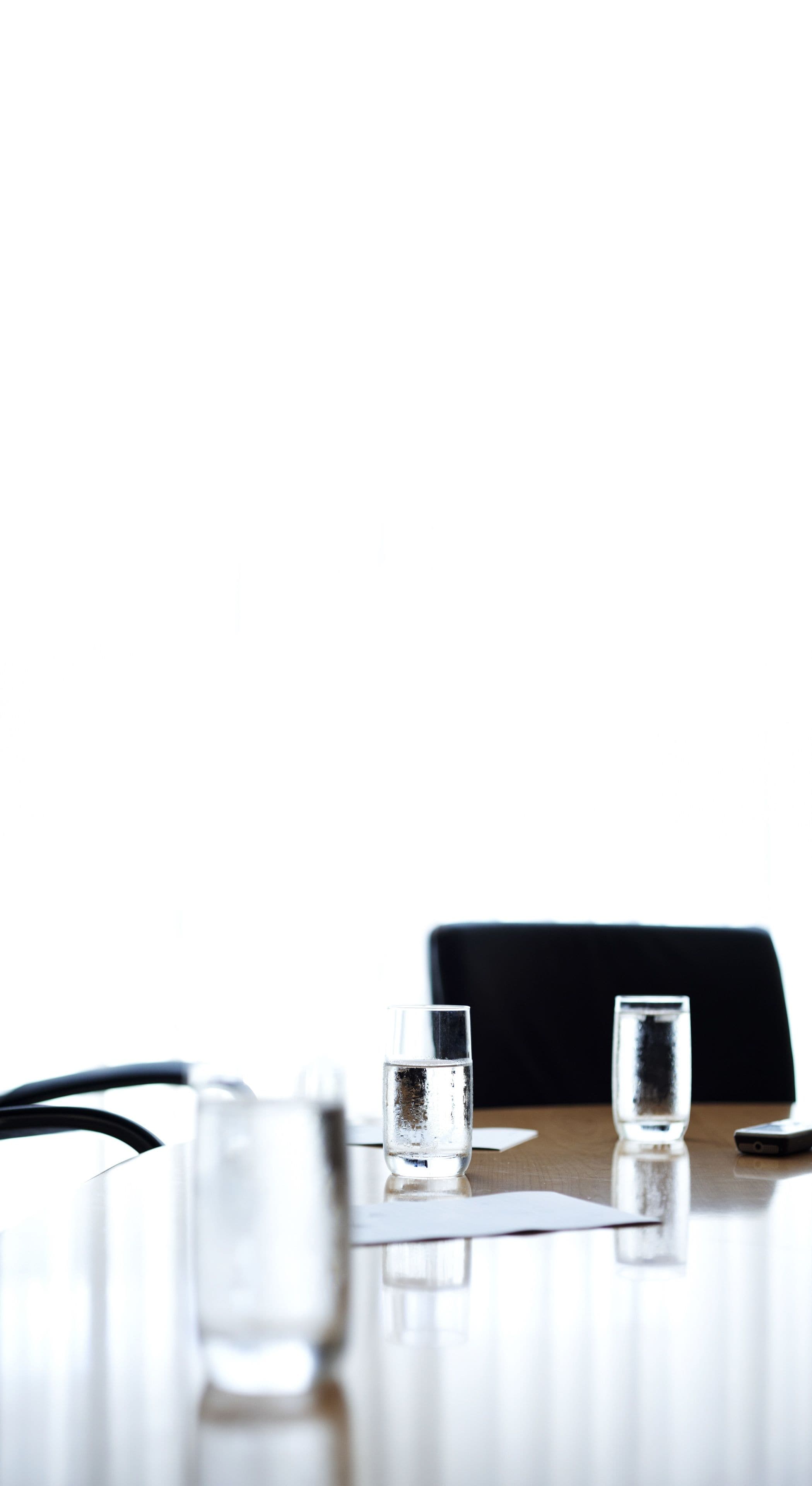Een tafel met twee glazen water, een smartphone en een zwarte stoel.
