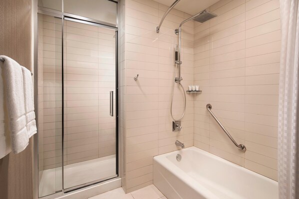 Un baño moderno con cabina de ducha de vidrio, bañera con barras de apoyo y ducha.