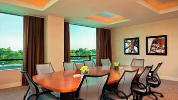 A conference room with a large table, six chairs, and two windows with curtains.