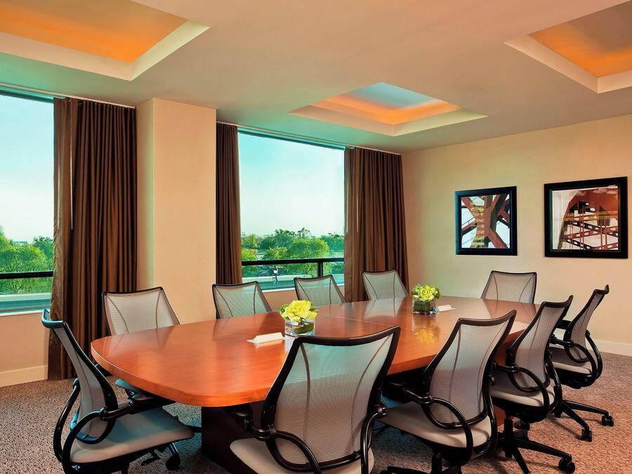 A conference room with a large table, six chairs, and two windows with curtains.