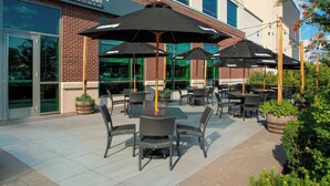 An outdoor patio with tables and chairs, umbrellas, and potted plants.