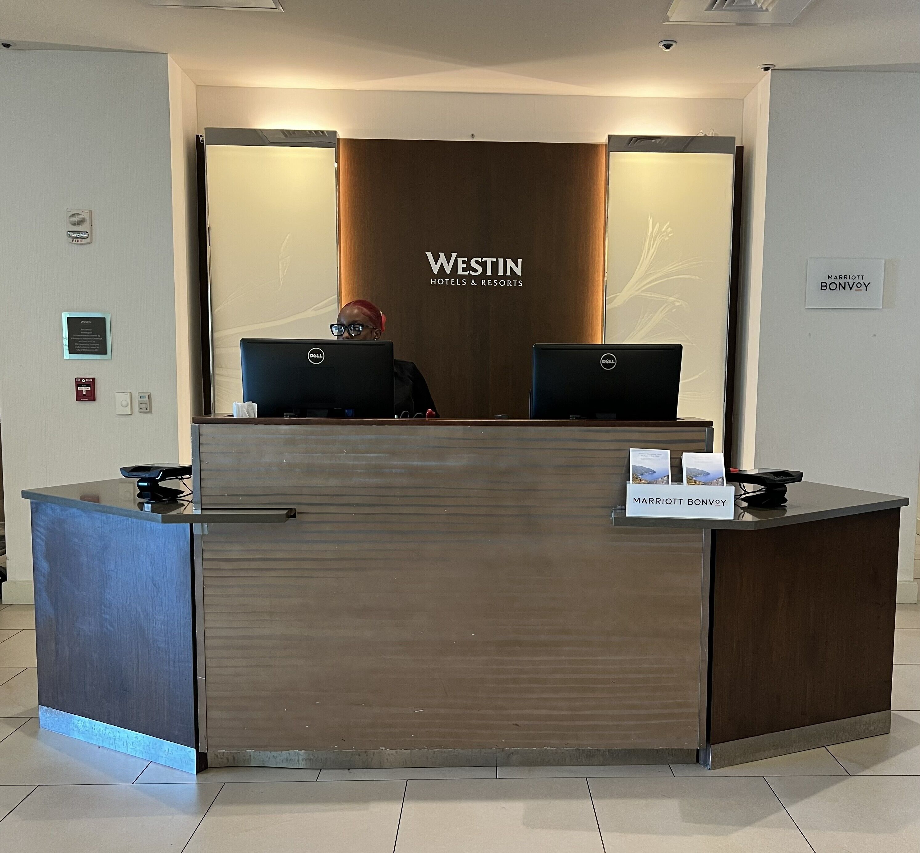 A reception desk at Westin Hotels & Resorts with two computers, a fire alarm, and a sign for Marriott Bonvoy.