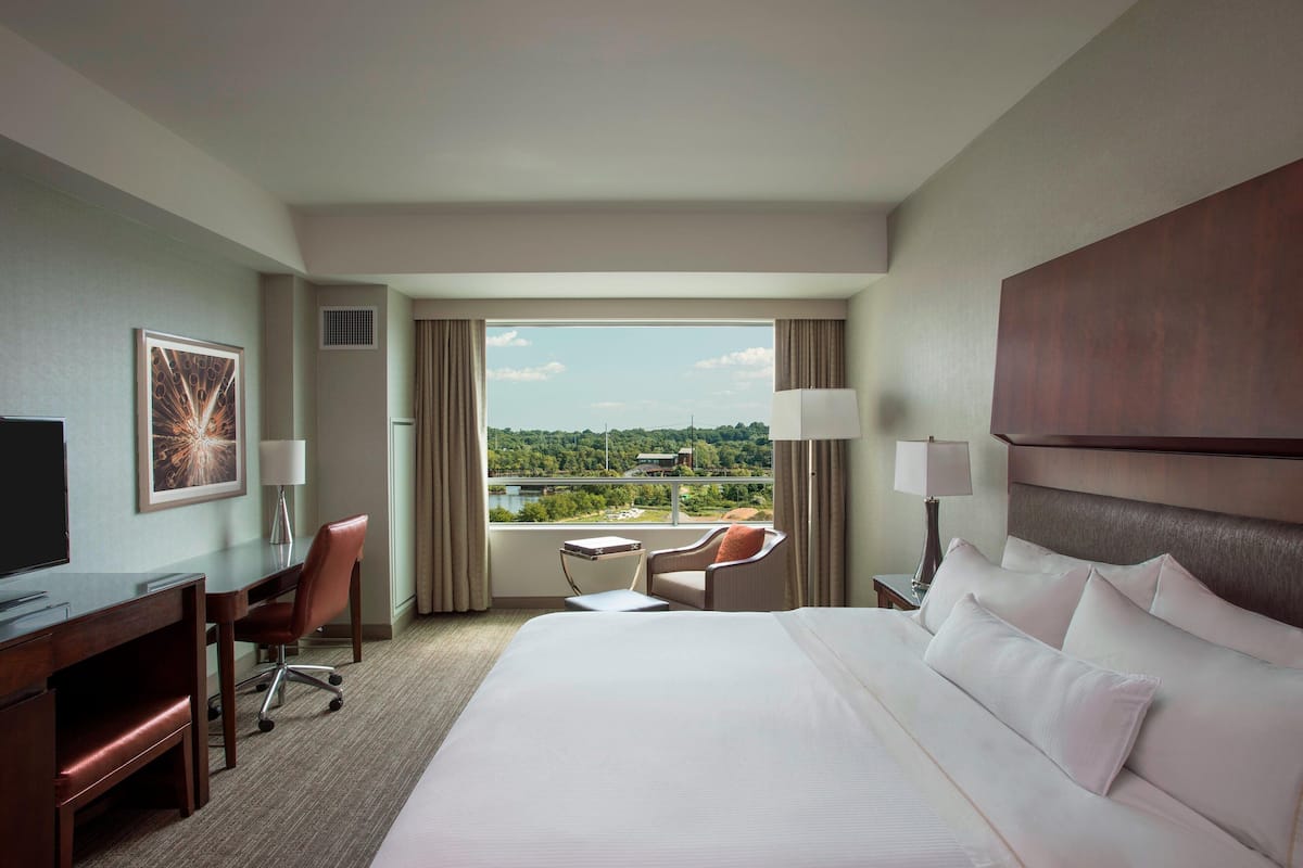 Habitación de hotel con una cama grande, un escritorio, una silla y vistas a un paisaje urbano.