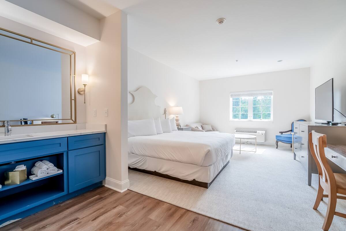 A bedroom with a large bed, a desk, a chair, a TV, and a window.