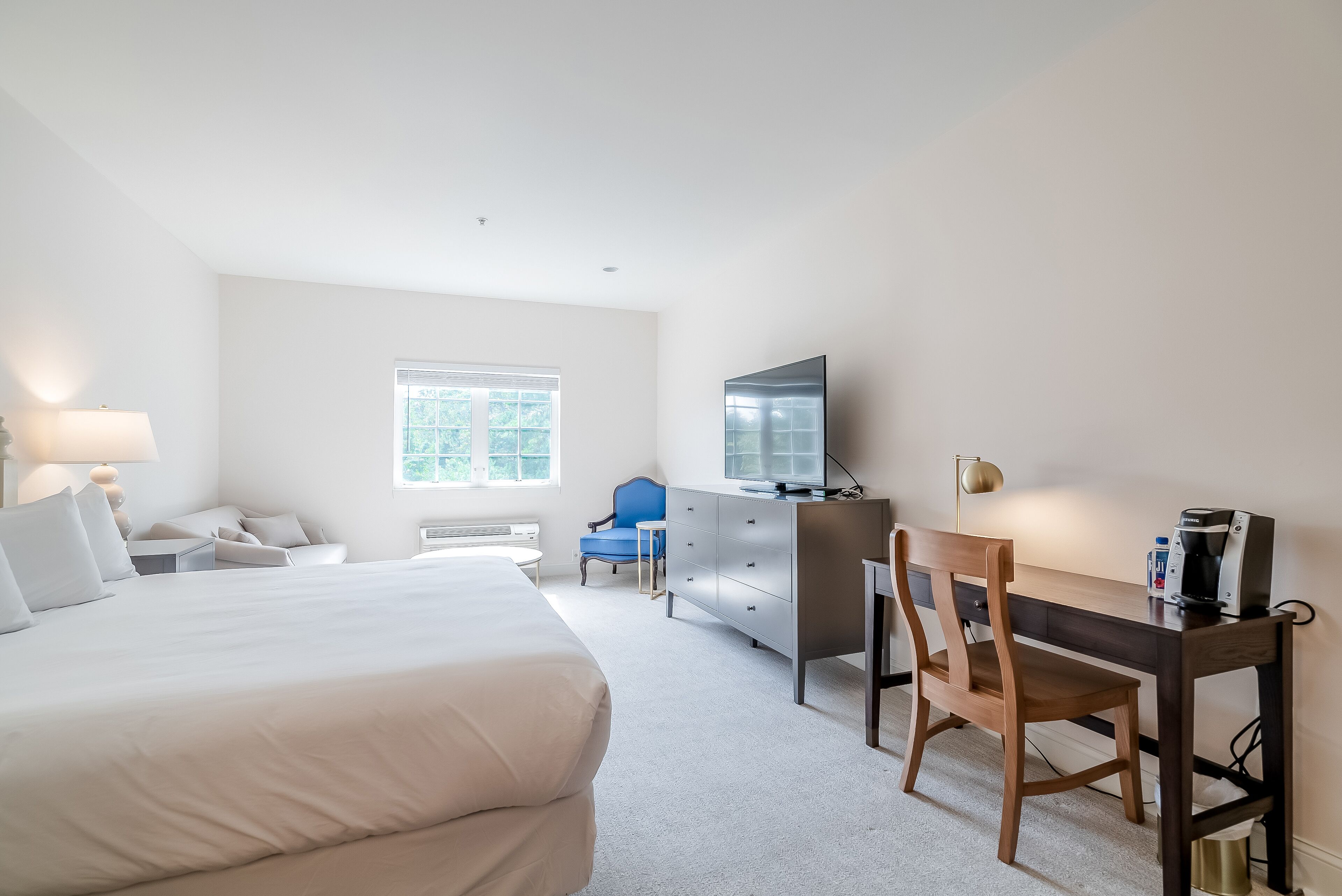 Une chambre d’hôtel avec un grand lit, un bureau avec une chaise, une commode, une télévision et une fenêtre.