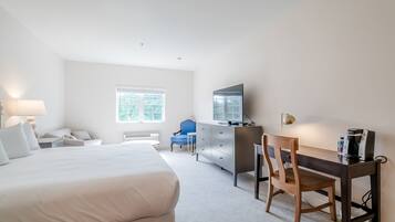 Une chambre d’hôtel avec un grand lit, un bureau avec une chaise, une commode, une télévision et une fenêtre.