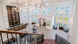 A spacious hotel lobby with a high ceiling, a central chandelier, a staircase, and a seating area with sofas. - Chateau Renault (Egg Harbor City)