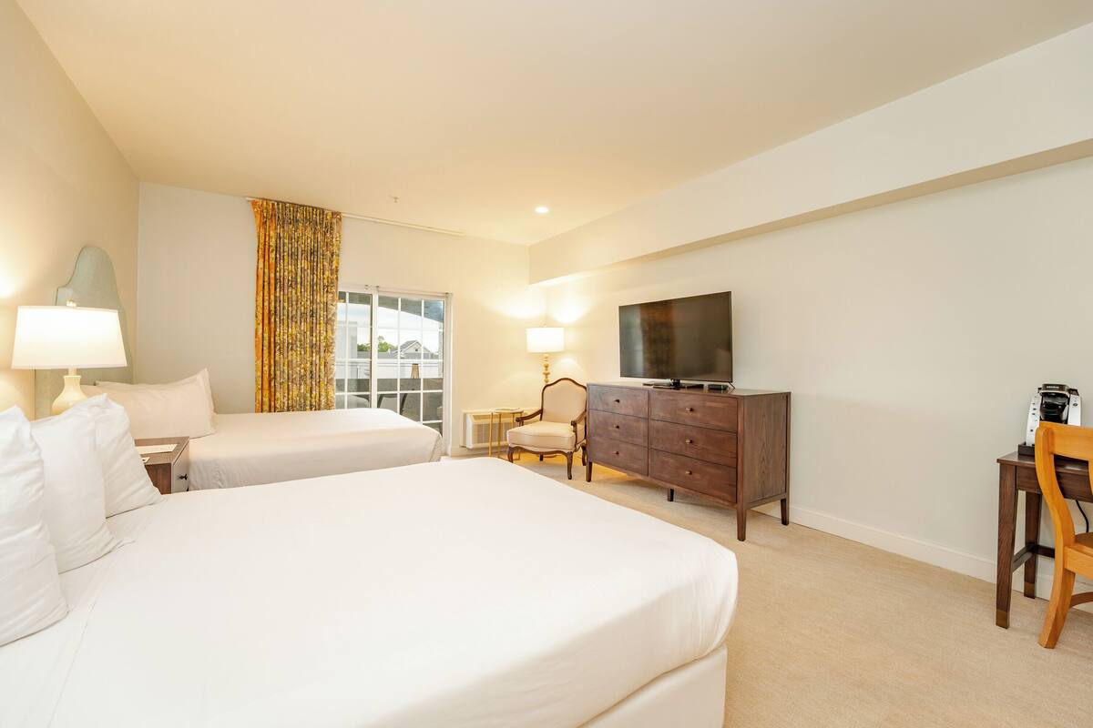 A hotel room with two beds, a TV, a dresser, a chair, and a desk.