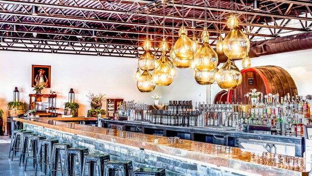 A bar area with a long counter, multiple stools, hanging light fixtures, and a variety of bottles and glasses. - Chateau Renault (Egg Harbor City)