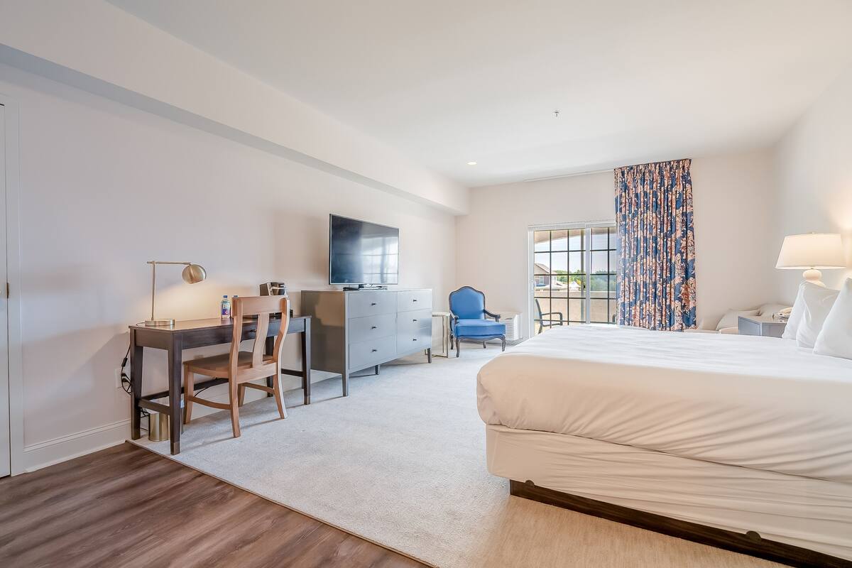 A hotel room with a bed, desk, chair, dresser, and a TV.
