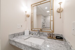 Un baño con lavamanos de mármol, un espejo grande y una ducha.