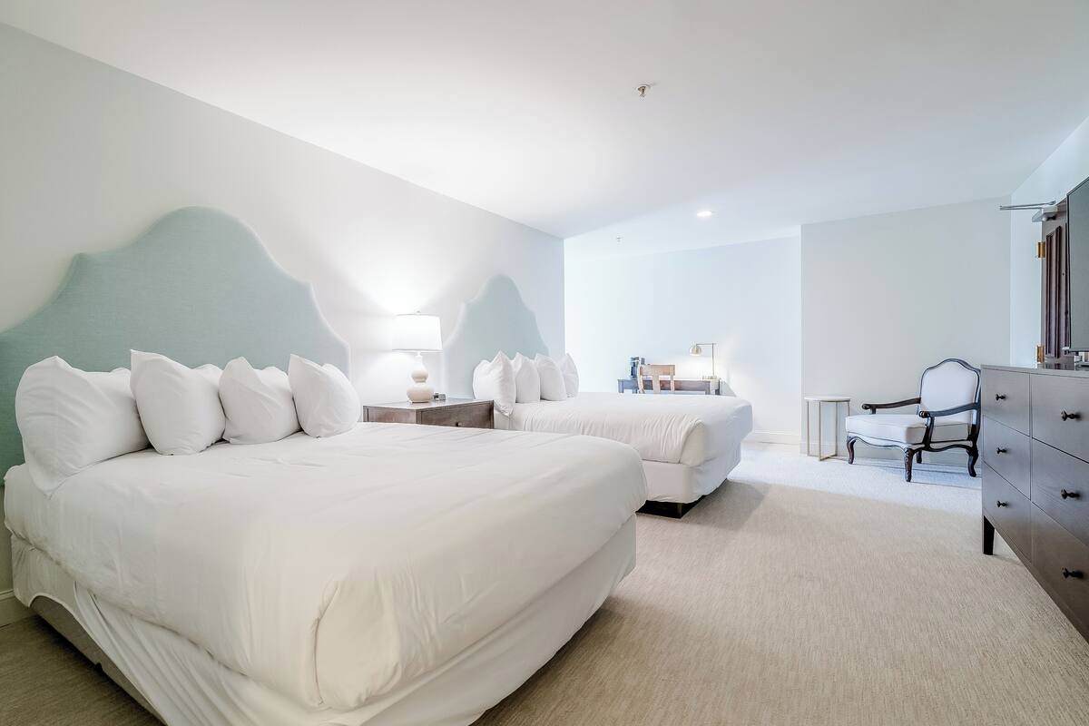 A modern hotel room with two beds, a dresser, a chair, and a desk.