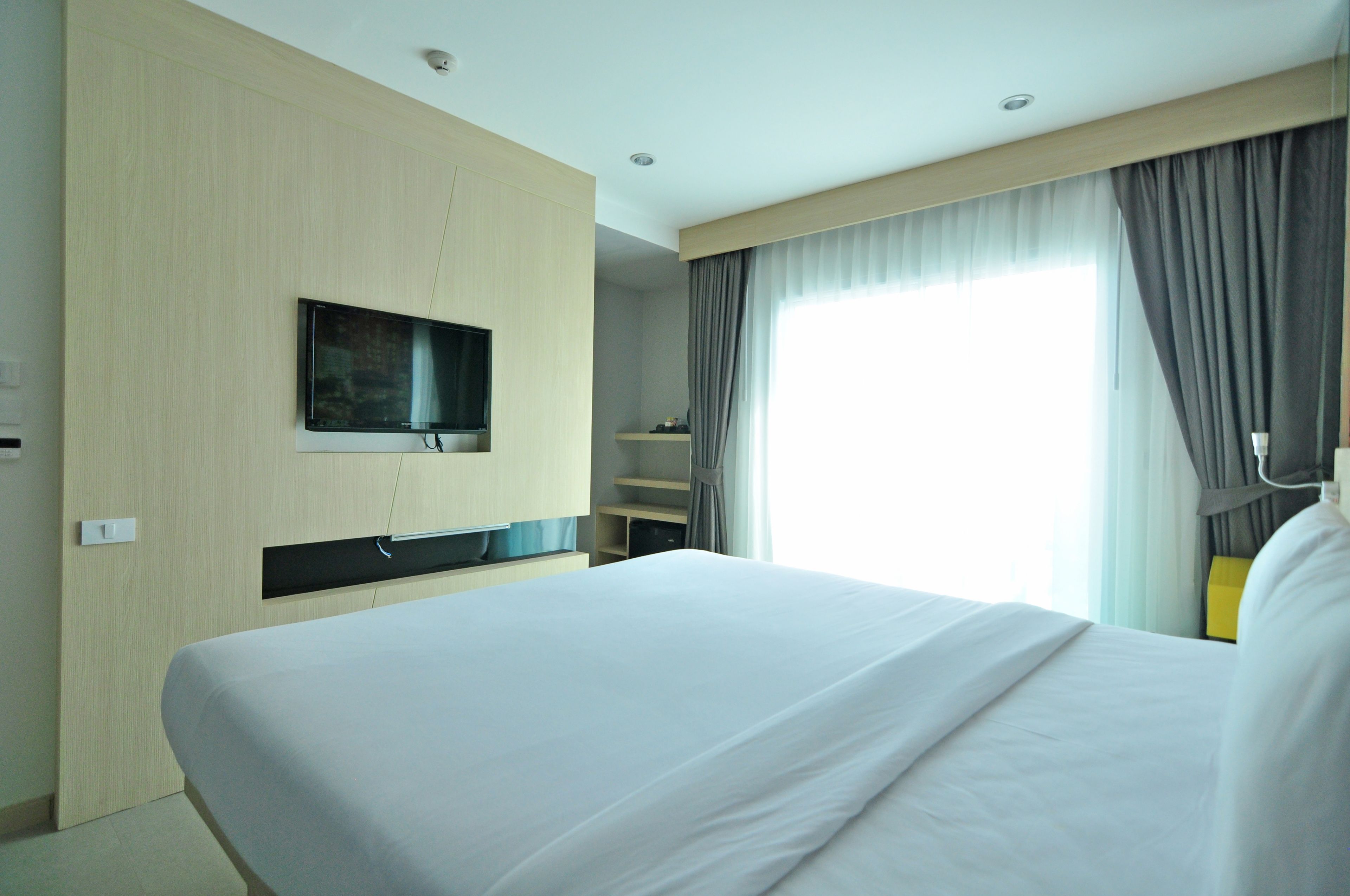 A hotel room with a large bed, a flat-screen TV mounted on the wall, and a window with curtains.