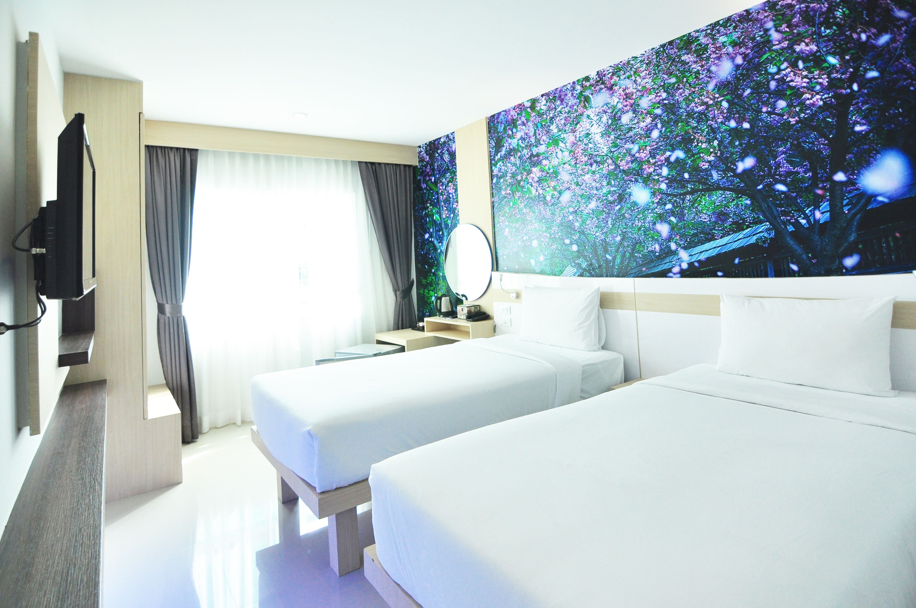 Une chambre d’hôtel avec deux lits, une télévision, une grande fenêtre avec des rideaux et une fresque murale.