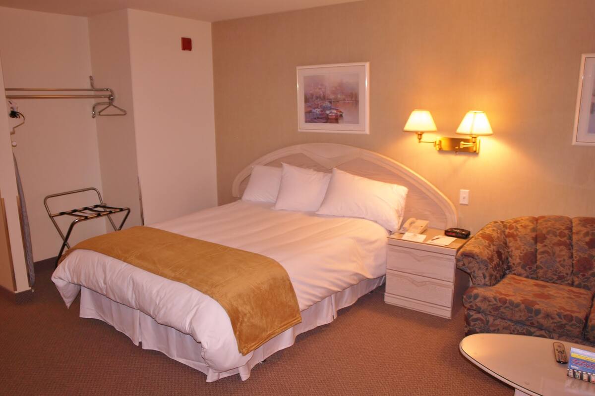 A hotel room with a bed, a chair, a nightstand, and two wall-mounted lamps.