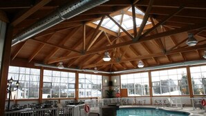 A covered pool area with wooden beams and large windows. - Auberge du Draveur (Maniwaki)