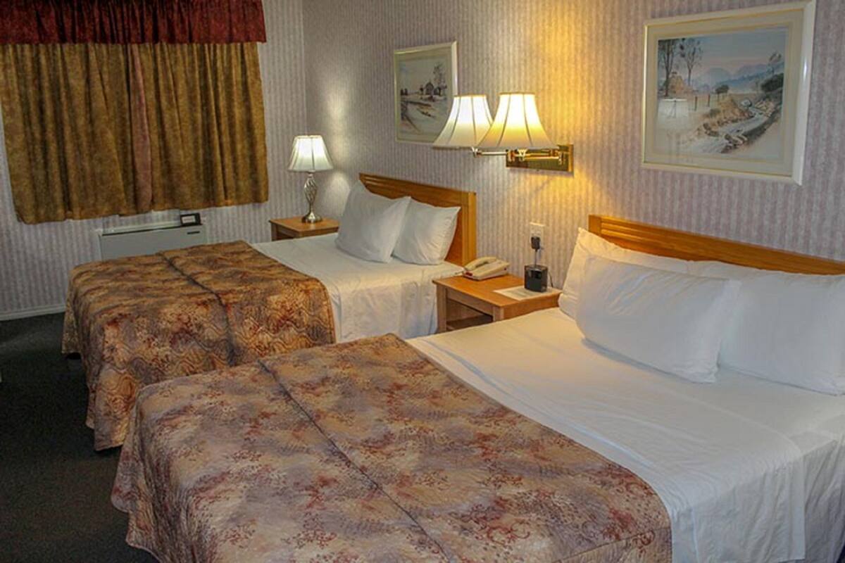 A hotel room with two beds, a nightstand with a lamp, a telephone, and two framed pictures on the wall.