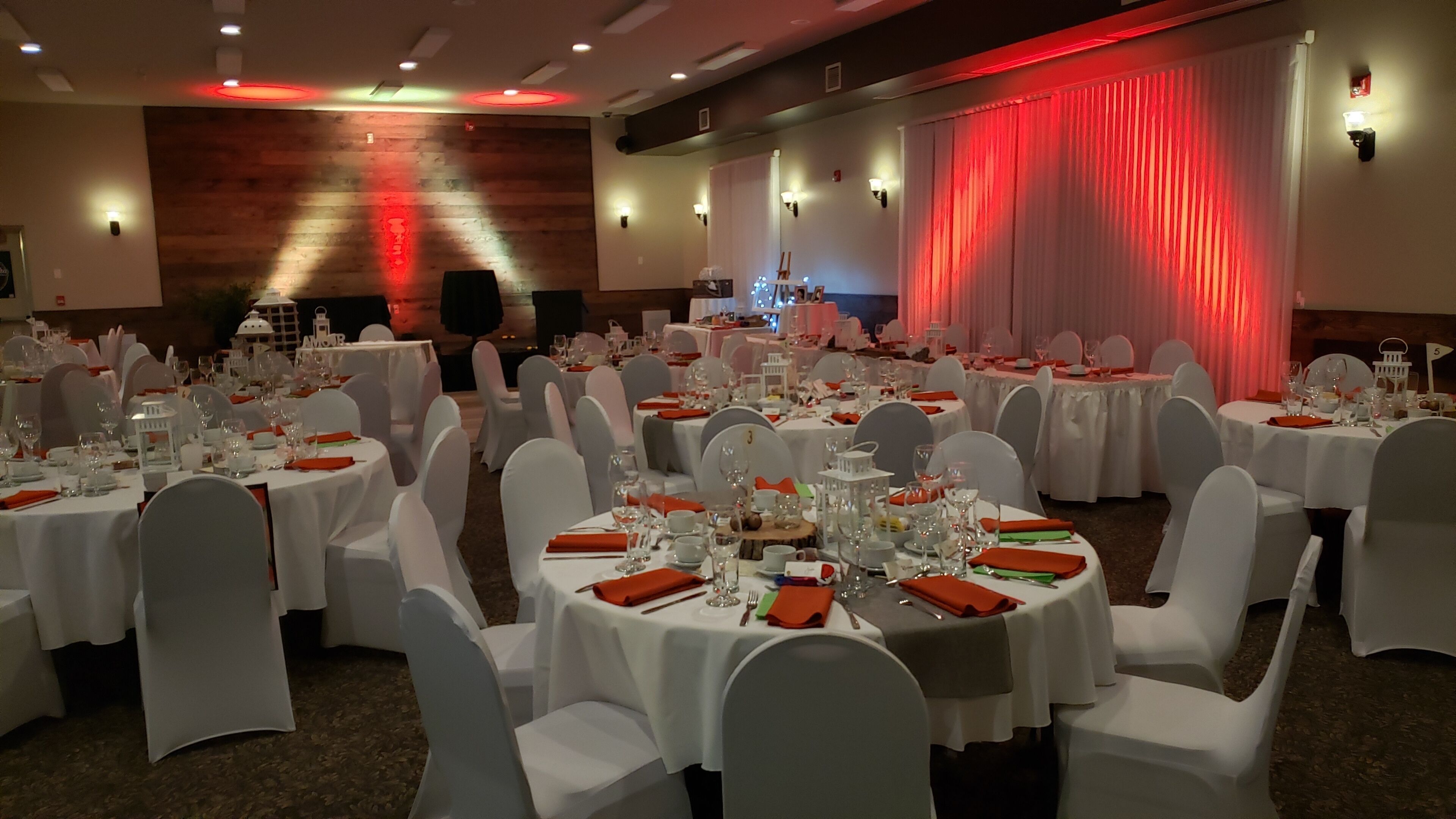 A banquet hall with round tables set for a formal event, white chairs, and a stage with red lighting.