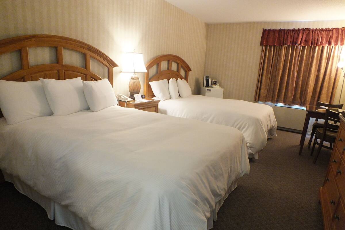 A hotel room with two large beds, a desk, a chair, a lamp, and a window with curtains.