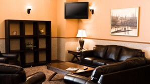 A living room with a leather sofa, a wooden coffee table, a bookshelf, a flat-screen TV, and a framed painting on the wall. - Auberge du Draveur (Maniwaki)