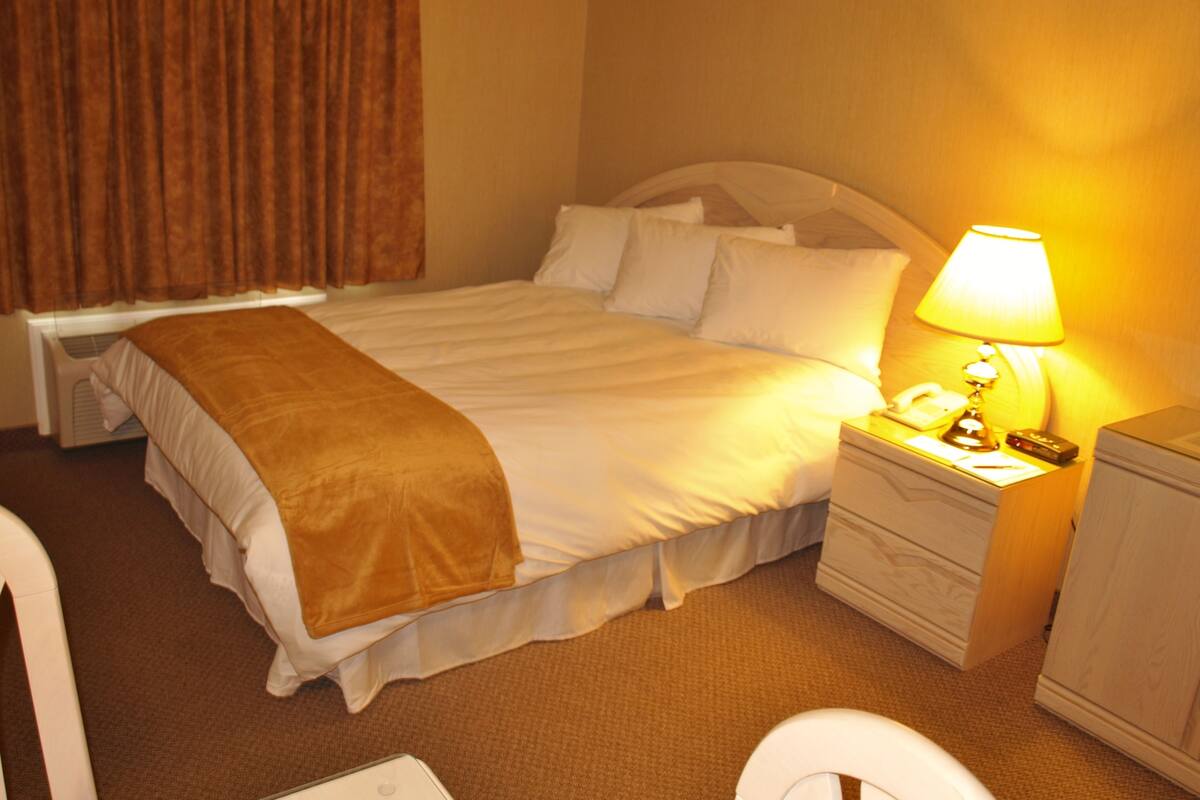 A hotel room with a bed, bedside table with a lamp, a telephone, and a small cabinet.