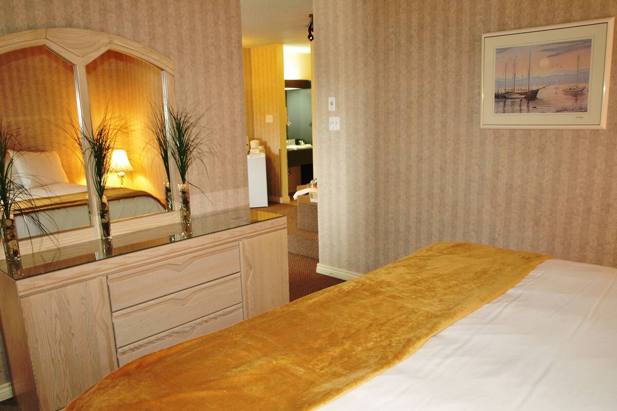 A hotel room with a bed, a dresser, a mirror, and a painting on the wall.