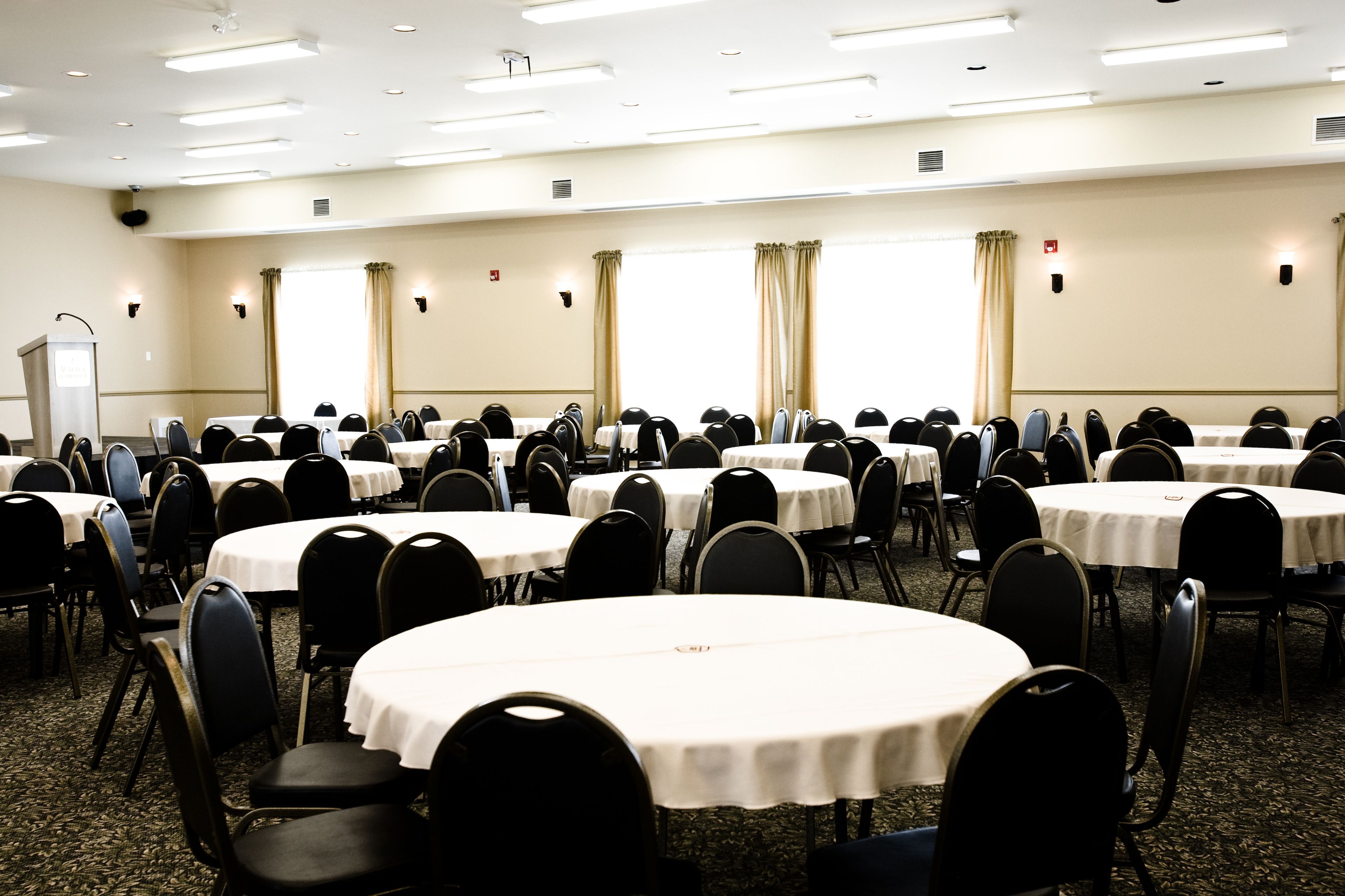 A conference room with multiple round tables and chairs, arranged in rows.