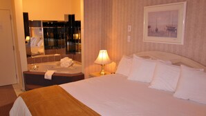 A hotel room with a large bed, a sitting area with a sofa, a bathtub, and a mirror. - Auberge du Draveur (Maniwaki)
