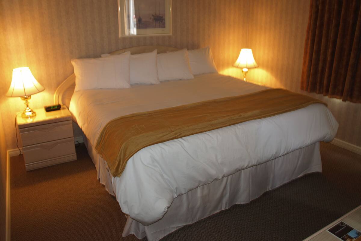 A hotel room with a large bed, two bedside tables with lamps, a framed picture on the wall, and a brown curtain.