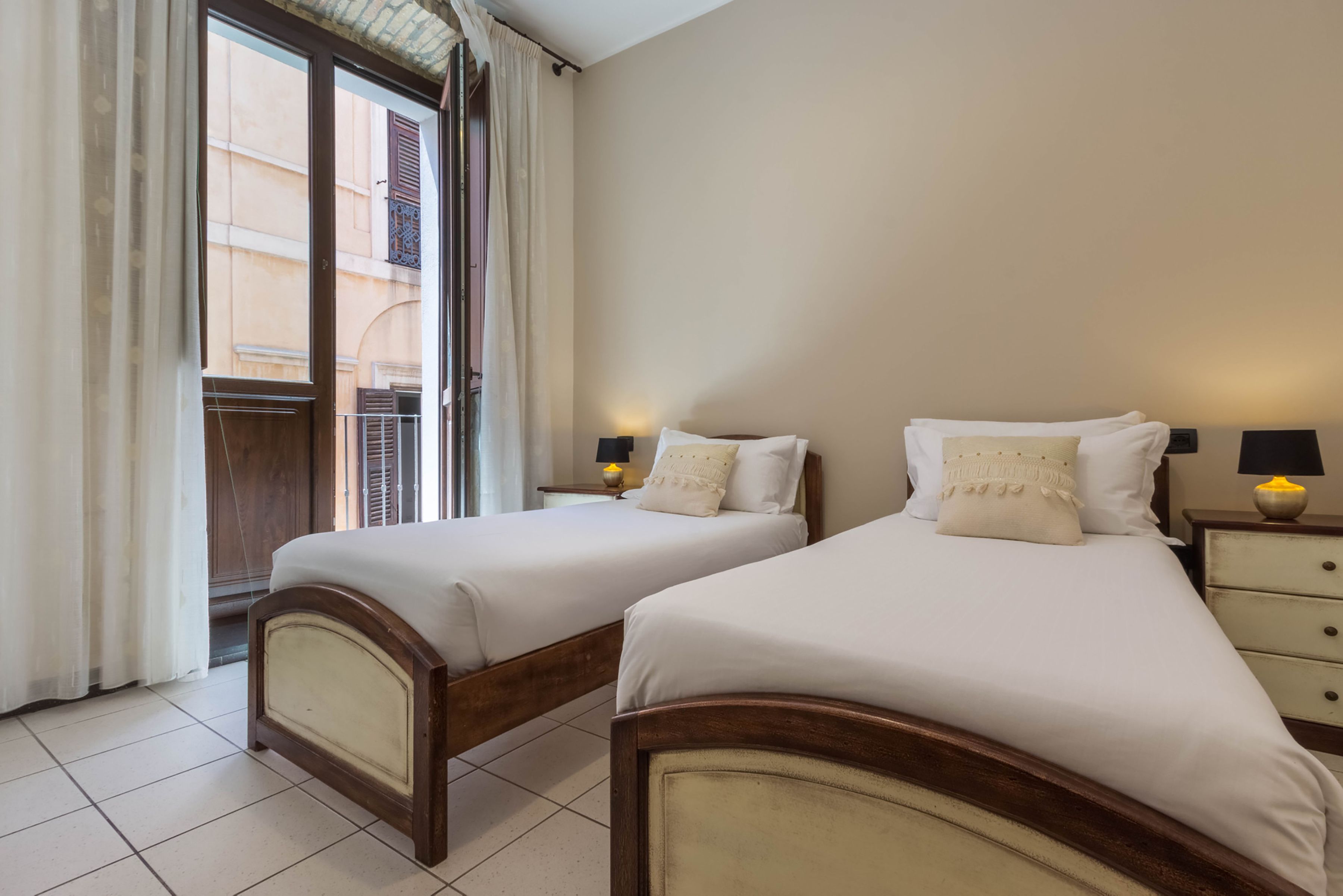 A hotel room with two beds, a window with curtains, and a view of a building outside.